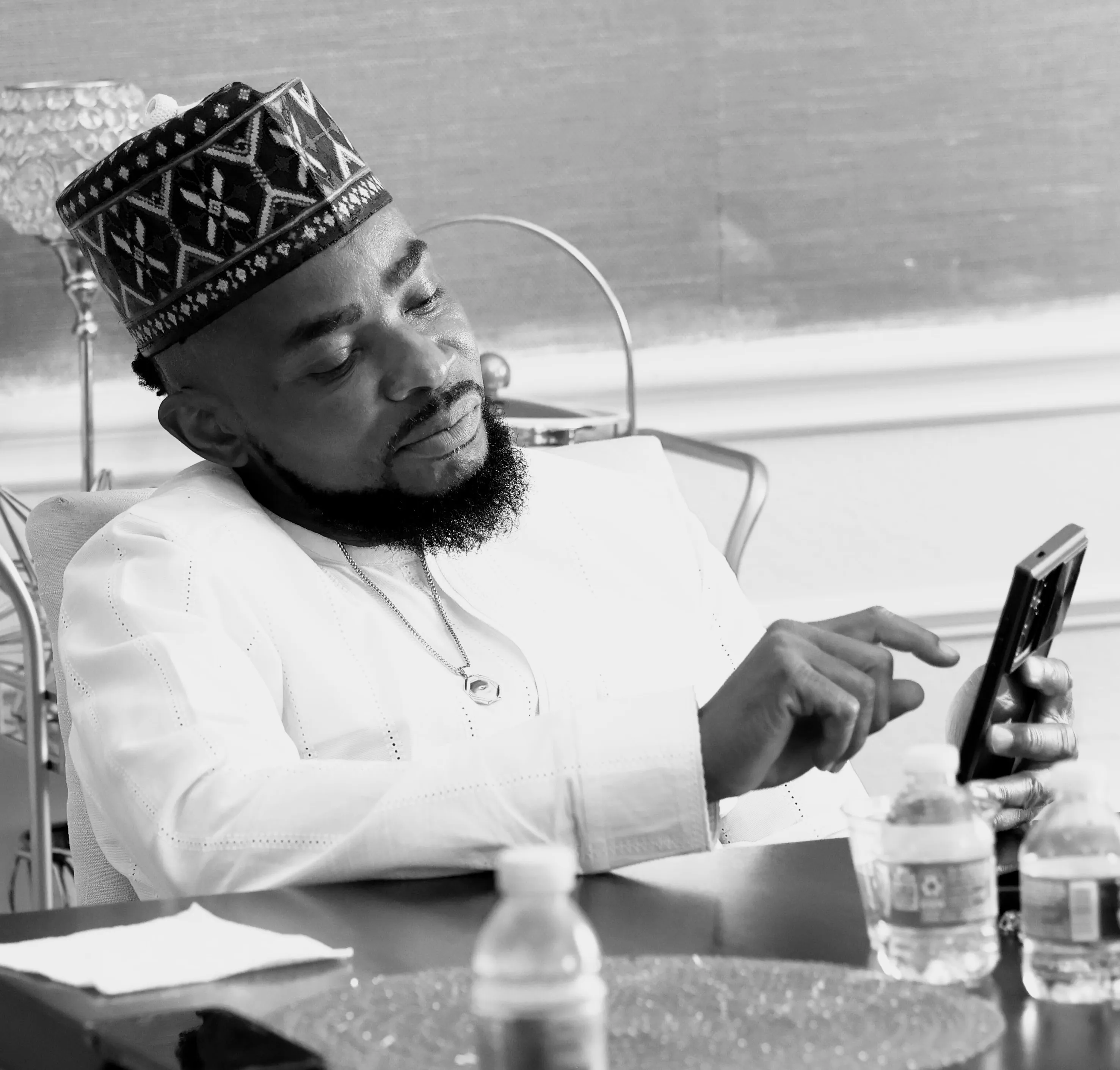 B&W lifestyle portrait - man in kufi looking at phone at desk